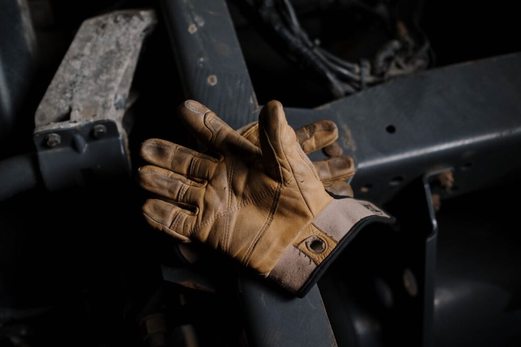 Close-up of worn leather gloves resting on machinery, suggesting hard work.